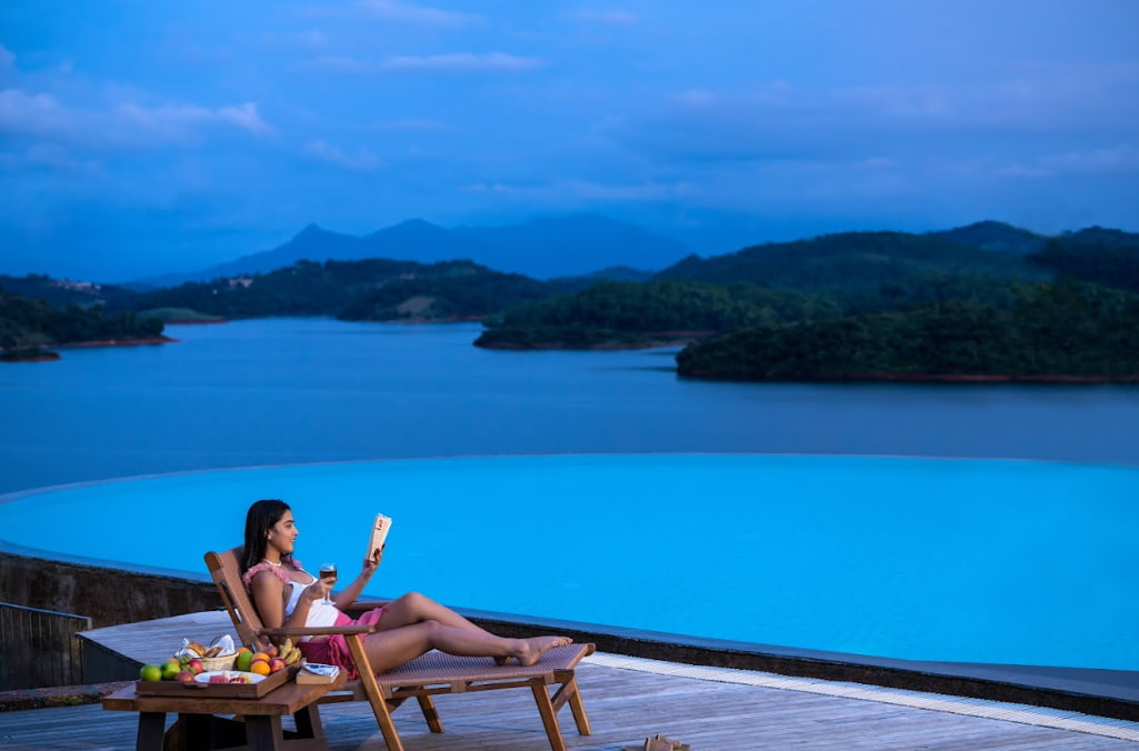Woman reading a book sitting next to a swimming pool at Mountain Shadows resort in Wayanad